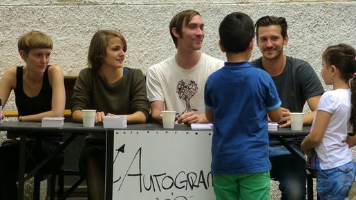 Kinder stehen vor einem Tisch, an dem eine Band Autogramme gibt