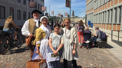 Mädchen und Kulturlotsin stehen mit einem Paar in traditioneller Kleidung vor dem Karlsruher Schloss um eine Stadtführung zu machen